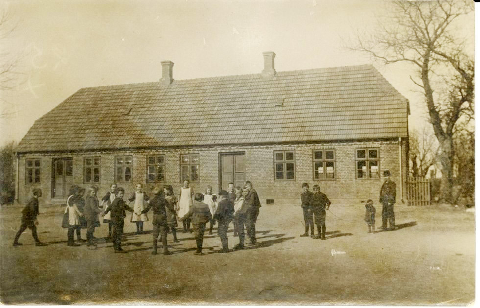 Børnene i Hem Hovedskole leger sangleg ca. 1910. Til højre står førstelærer P.J. Poulsen og sønnen Aksel, der leger med to ”heste”.